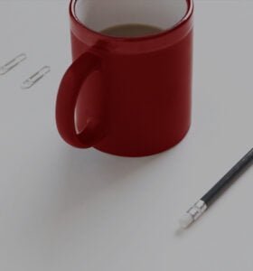 Red mug on desk next to pencil and paperclips