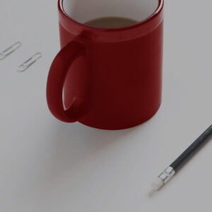 Red mug on desk next to pencil and paperclips