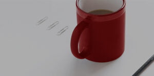 Red mug on desk next to pencil and paperclips