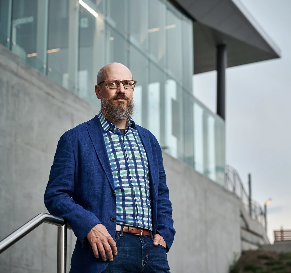 Portrait of Michael Spratt leaning on metal railing in front of industrial building
