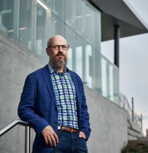 Portrait of Michael Spratt leaning on metal railing in front of industrial building