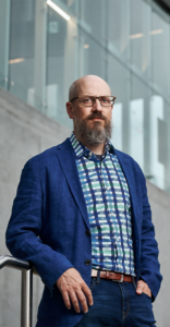 Portrait of Michael Spratt leaning on metal railing in front of industrial building
